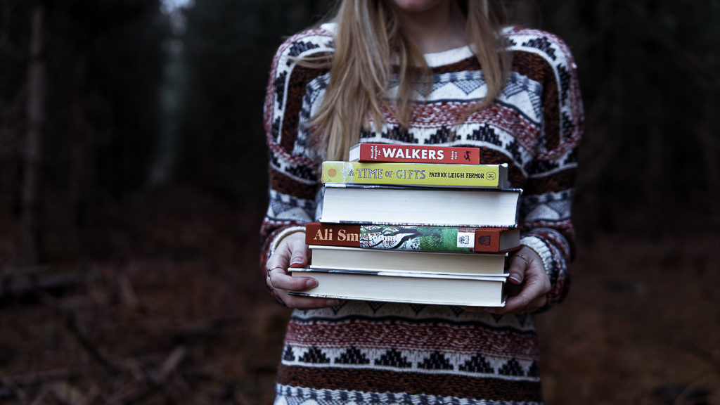 Photo of Nell holding a selection of our favourite outdoor books to inspire walking wanderlust.