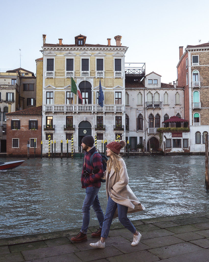 Couple walking along the grand canal near Rialto Bridge in Venice with palazzo in background
