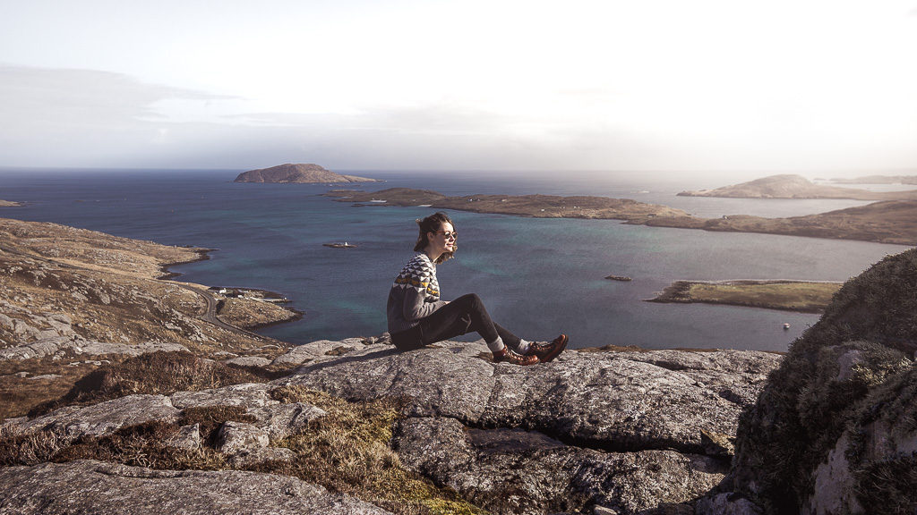 Nell sitting atop the Isle of Barra in the Outer Hebrides with Danner boots on and the backdrop of the Atlantic Ocean.