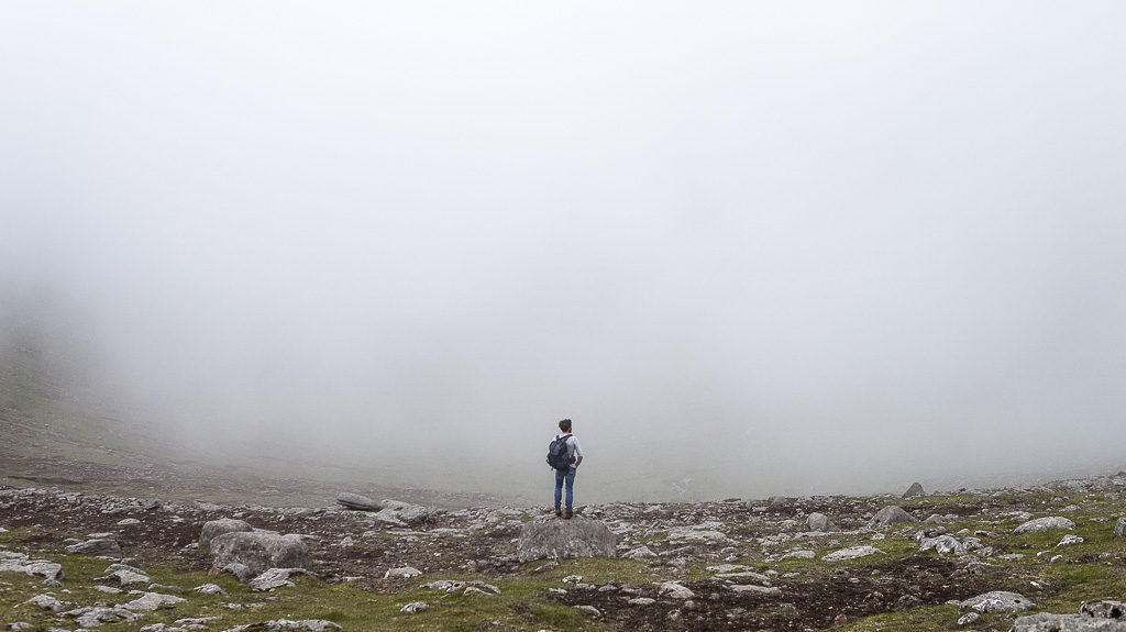 Luke atop a mountain whilst hiking on the Faroe Islands, with a wall of mist ahead.