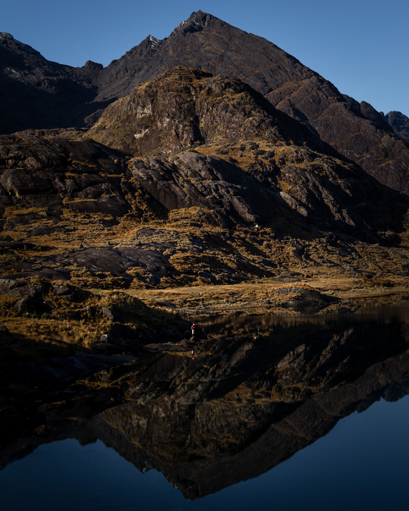 Luke standing alongside Loch Coruisk with a perfect reflection