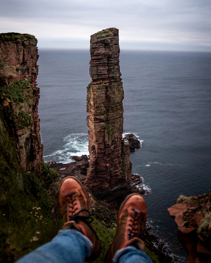 Luke sitting on the edge of the cliff with Old Man of Hoy sea stack directly below